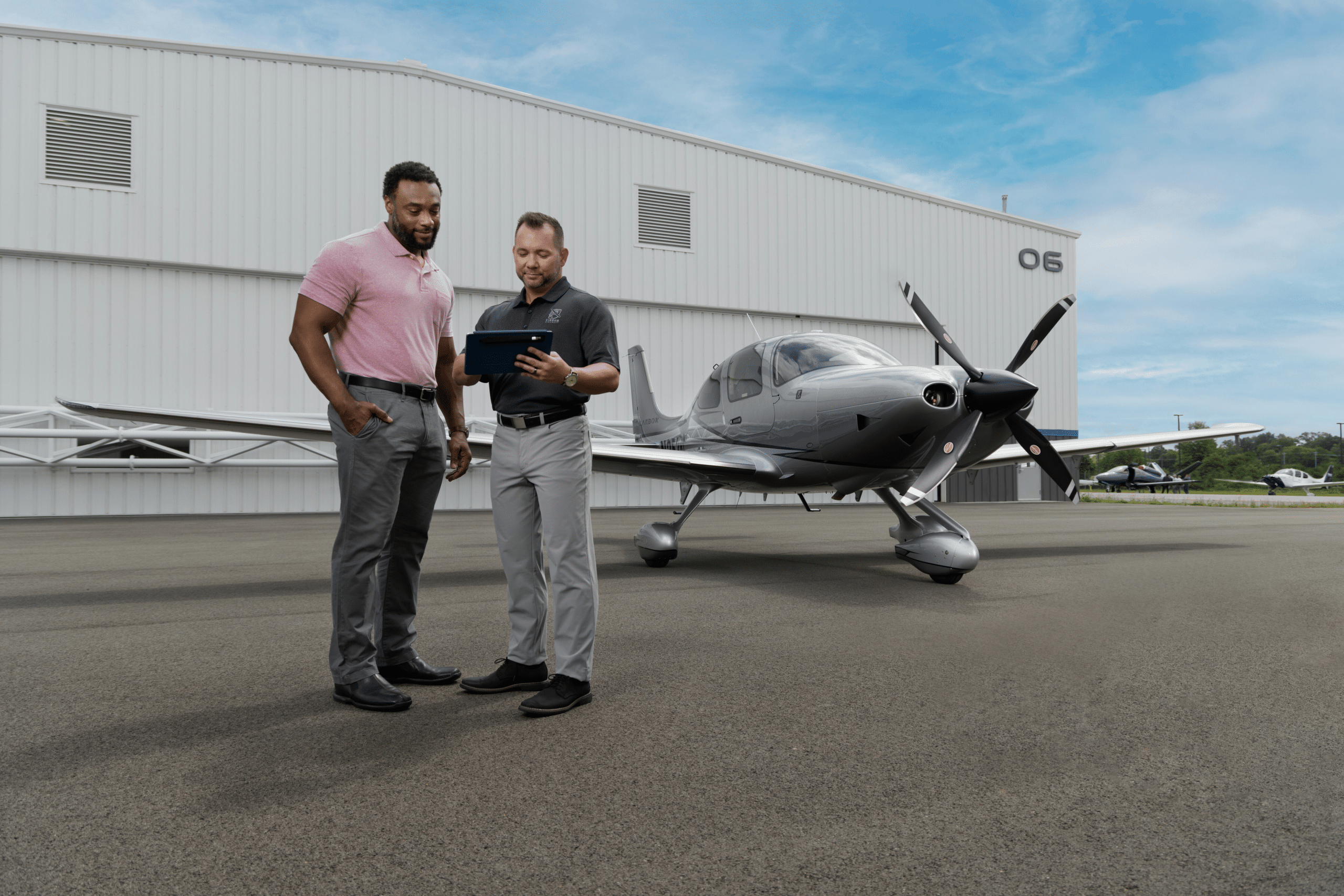 people looking at a tablet in front of a cirrus airplane